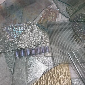 May include: A pile of various textured glass pieces in shades of clear, white, and gold. The glass pieces are arranged in a random pattern, creating a visually interesting composition.