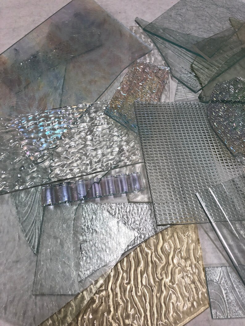 May include: A pile of various textured glass pieces in shades of clear, white, and gold. The glass pieces are arranged in a random pattern, creating a visually interesting composition.