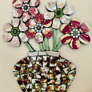 Könnte beinhalten: Eine Mosaikvase mit Blumenmuster. Die Vase ist aus zerbrochenen Porzellanteilen gefertigt und mit roten, weißen und grünen Blumen verziert.