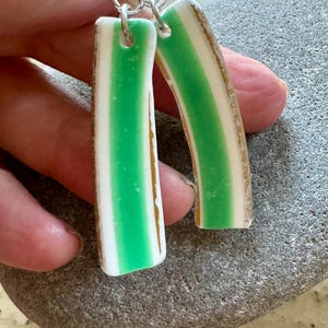 May include: A pair of green and white striped earrings with gold accents. The earrings are made of ceramic and have a unique, handmade look.