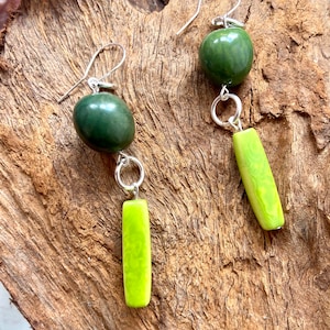 May include: A pair of green and lime green dangle earrings with silver hooks and connecting rings. The earrings feature a round green bead and a long rectangular lime green bead.