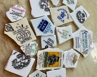 Könnte beinhalten: Eine Sammlung zerbrochener Keramikstücke mit verschiedenen Logos und Designs. Die Stücke beinhalten Logos für IKEA, Royal Albert, Dunnoon und mehr. Die Stücke liegen auf einer hellbraunen Oberfläche.