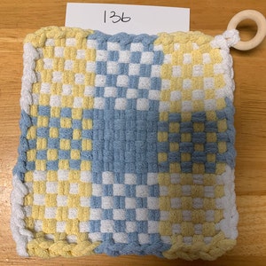 May include: A blue and yellow woven pot holder with a white woven border. The pot holder has a loop on one corner.