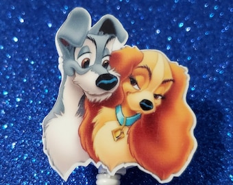 May include: A white retractable badge holder with a cartoon image of Lady and the Tramp. The image shows Lady and Tramp looking at each other with their heads touching. Lady is a brown and white dog with a blue collar. Tramp is a gray and white dog.