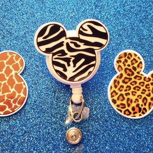 May include: Three Mickey Mouse-shaped retractable badge holders with different animal print designs: zebra, giraffe, and leopard.