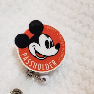 May include: Red and white circular badge with a cartoon image of Mickey Mouse and the text "WALT DISNEY WORLD PASSHOLDER".