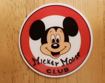May include: A red and white circle sticker with a cartoon image of Mickey Mouse's face and the text "Mickey Mouse Club".
