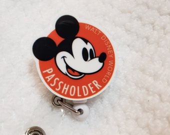 May include: Red and white circular badge with a cartoon image of Mickey Mouse and the text "WALT DISNEY WORLD PASSHOLDER".