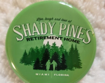 May include: Green button with the text "Live, laugh and love at Shady Pines Retirement Home" and the text "Miami Florida" at the bottom. The button has a silhouette of two people walking in a forest.