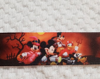 May include: A Halloween-themed ribbon featuring Mickey Mouse, Donald Duck, and Goofy in costumes. The ribbon has a dark orange background with silhouettes of trees and a full moon. The characters are holding pumpkins and are surrounded by fall leaves.