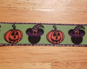 May include: Green ribbon with a repeating pattern of orange jack-o'-lanterns and black witch hats with purple accents. The ribbon has a thin black border and is suitable for Halloween crafts and decorations.