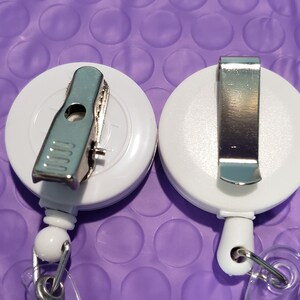 May include: Two white retractable badge holders with metal clips. One clip is a spring clip and the other is a belt clip.