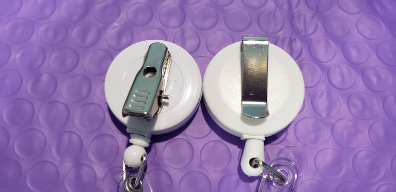 May include: Two white retractable badge holders with metal clips. One clip is a spring clip and the other is a belt clip.