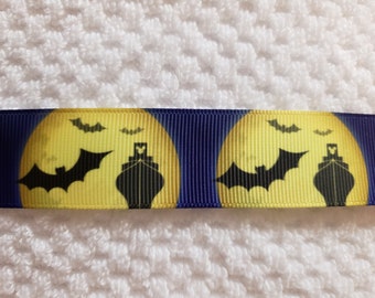 May include: A dark blue ribbon with a repeating Halloween-themed pattern. The design features a yellow full moon with a black bat silhouette, a ship, and smaller bats. The ribbon is set against a white, textured background.