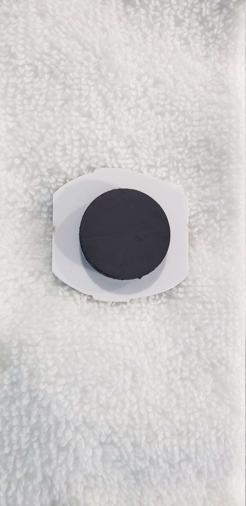 May include: A white plastic magnetic hook with a black round magnet. The hook is designed to hold items on a metal surface.