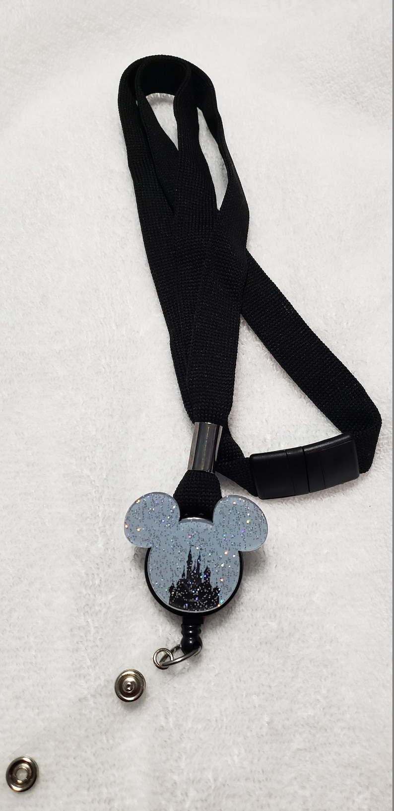 May include: Black lanyard with a retractable badge holder featuring a silver glitter Mickey Mouse head with a silhouette of Cinderella's castle inside.