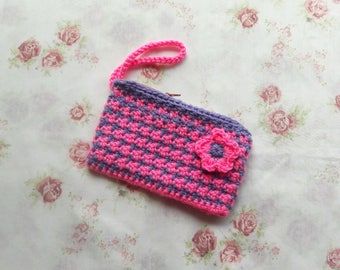 May include: A small crocheted purse with a pink and purple chequered pattern and a pink flower accent. The purse has a handle and a zipper closure.