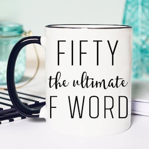 May include: White coffee mug with a black handle and black rim. The mug has black text that reads "FIFTY the ultimate F WORD".