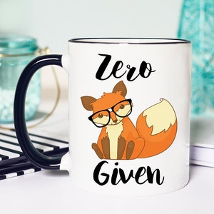 May include: White ceramic mug with a black rim and handle. The mug features a cartoon fox wearing glasses and the text "Zero Given".