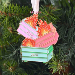 May include: A Christmas ornament shaped like three overflowing dumpsters on fire. The dumpsters are pink, red, and green and have the years 2020, 2021, and 2022 written on them.