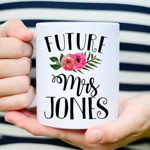 May include: White ceramic mug with black text that reads "Future Mrs. Jones" and a pink floral design.