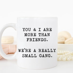 May include: White ceramic coffee mug with black text that reads "You & I are more than friends. We're a really small gang."