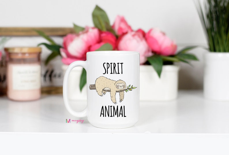 May include: White ceramic coffee mug with a black and white illustration of a sloth hanging from a branch. The text "SPIRIT ANIMAL" is printed on the mug.