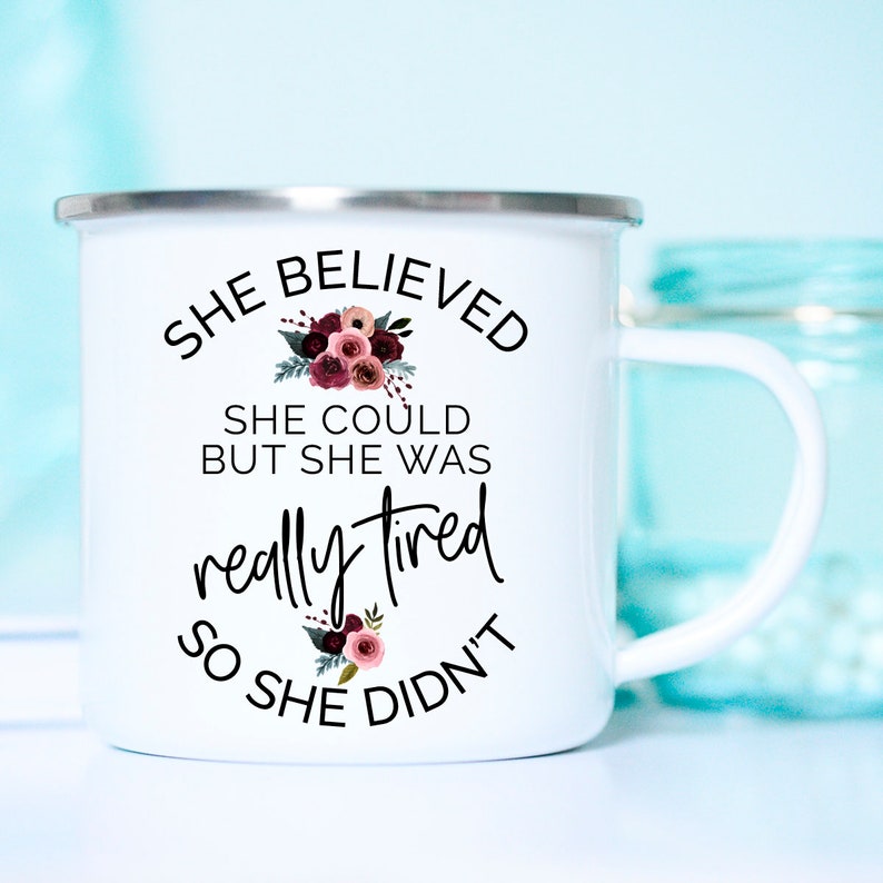 May include: White enamel mug with a silver rim and a curved handle. The mug features the text "SHE BELIEVED SHE COULD BUT SHE WAS REALLY TIRED SO SHE DIDN'T" in black script, with floral accents in burgundy and pink.