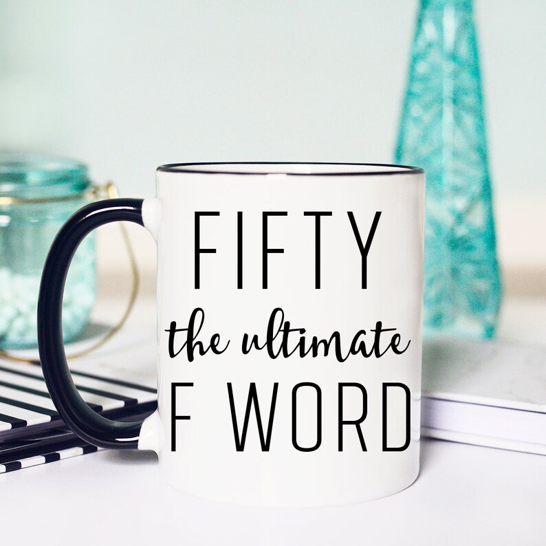 May include: White coffee mug with a black handle and black rim. The mug has black text that reads "FIFTY the ultimate F WORD".