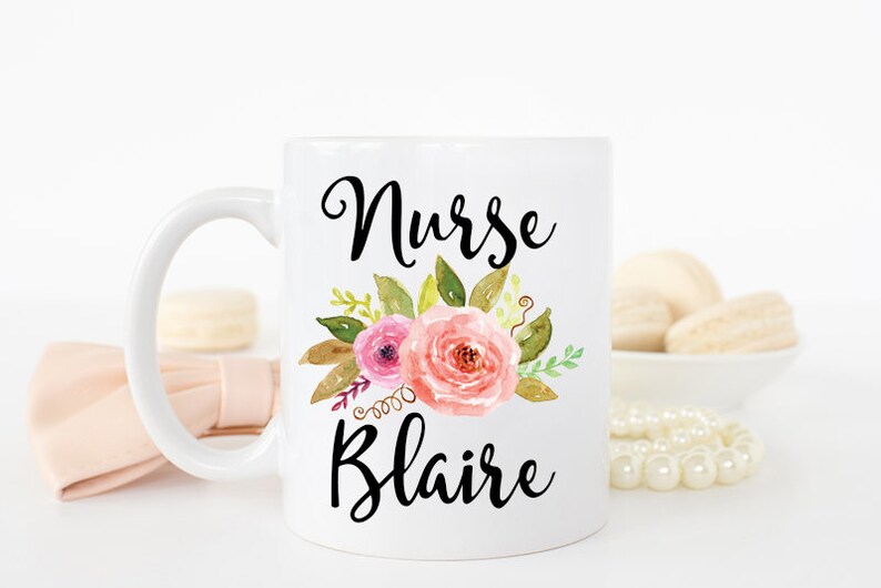 Puede incluir: Taza de cer&aacute;mica blanca con un dise&ntilde;o floral negro y el texto "Nurse Blaire".