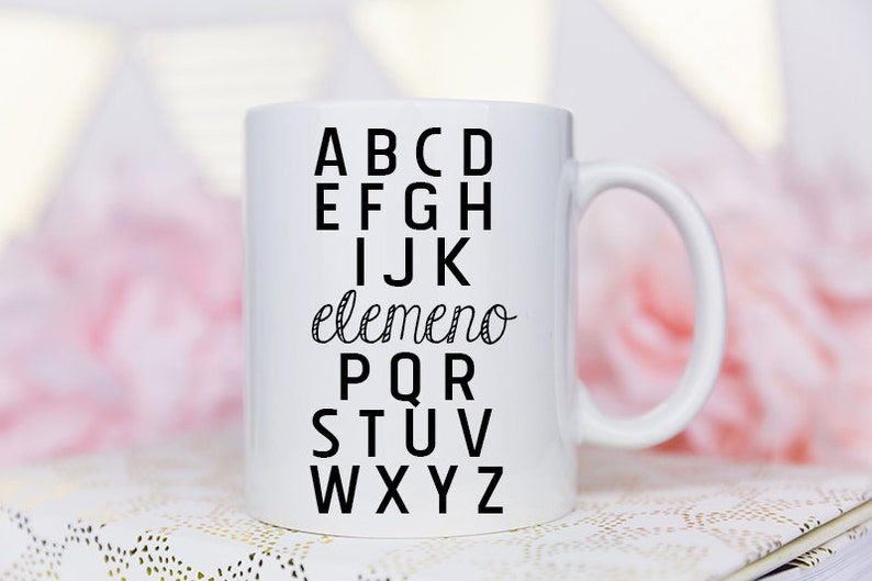 May include: White ceramic mug with a black design of the alphabet with the word "elemento" in cursive between the letters I and J.