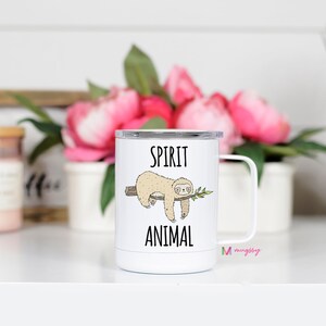 May include: White travel mug with a black and white illustration of a sloth hanging from a branch. The mug says "Spirit Animal" in black text.