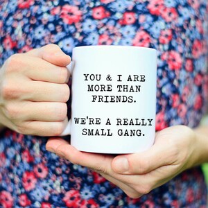 May include: White ceramic mug with black text that reads "You & I are more than friends. We're a really small gang."
