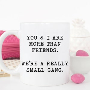May include: White ceramic coffee mug with black text that reads "You & I are more than friends. We're a really small gang."