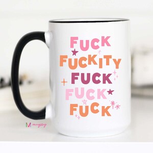 May include: White ceramic coffee mug with a black handle. The mug has a black rim and features the text "FUCK FUCKITY FUCK FUCK FUCK" in pink, orange, and purple with stars and sparkles.