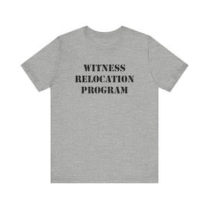 Op de afbeelding: Een grijs t-shirt met de tekst "WITNESS RELOCATION PROGRAM" in zwart gedrukt.