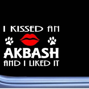 May include: A black and white sticker with the text "I kissed an Akbash and I liked it". The sticker features a red lip print and two paw prints.
