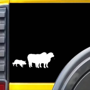 May include: White silhouette decal of a sheepdog herding three sheep on a black background. The decal is on the back window of a yellow vehicle.