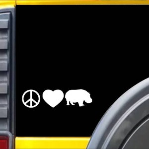 May include: A white peace sign, heart, and hippopotamus silhouette decal on a black background. The decal is on the back window of a yellow vehicle.