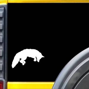 May include: White vinyl decal of a fox jumping, on a black background. The decal is on the back window of a yellow vehicle.