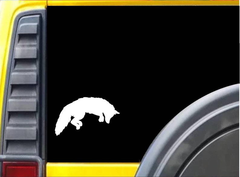 May include: White vinyl decal of a fox jumping, on a black background. The decal is on the back window of a yellow vehicle.