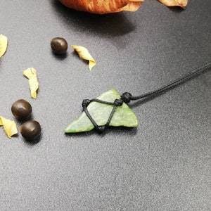 Pu&ograve; includere: Un ciondolo in pietra verde a forma di pinna di squalo, con un cordino nero.