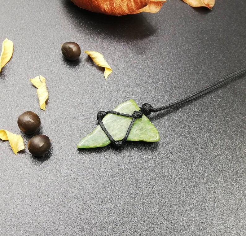 Pu&ograve; includere: Un ciondolo in pietra verde a forma di pinna di squalo, con un cordino nero.