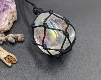 May include: A rainbow iridescent crystal is encased in a black macrame knot pendant. The crystal is a teardrop shape and is suspended from a black cord.