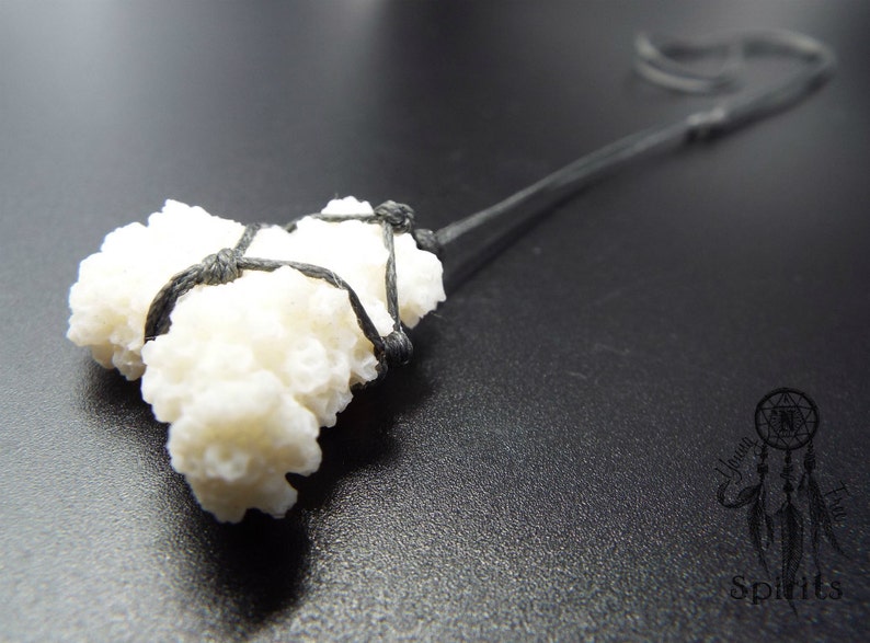 May include: A white coral pendant tied with black cord. The coral is a cluster of small, white, textured pieces. The cord is tied in a knot at the top of the pendant.