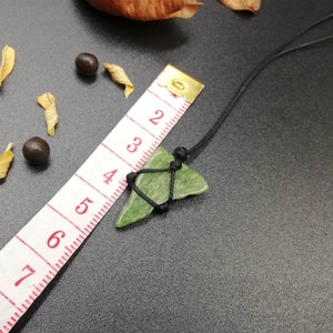 Pu&ograve; includere: Un ciondolo di pietra verde su un cordoncino nero. La pietra ha una forma irregolare e una texture ruvida. Il cordoncino &egrave; annodato nella parte superiore del ciondolo.