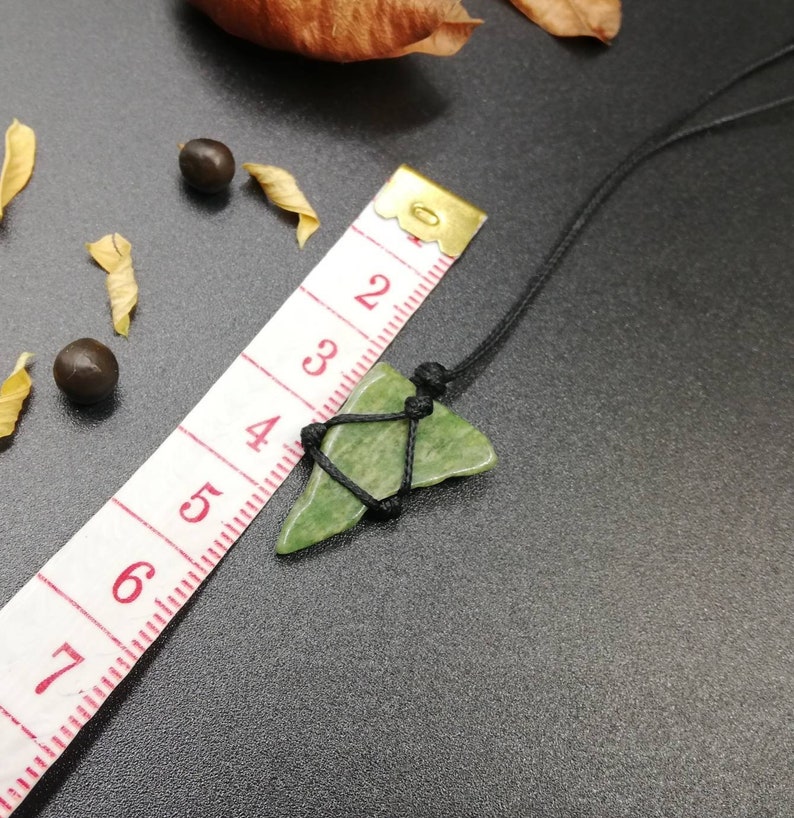 Pu&ograve; includere: Un ciondolo di pietra verde su un cordoncino nero. La pietra ha una forma irregolare e una texture ruvida. Il cordoncino &egrave; annodato nella parte superiore del ciondolo.