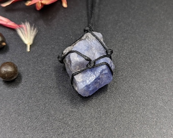 May include: A blue crystal pendant wrapped in black cord, hanging from a black cord necklace.