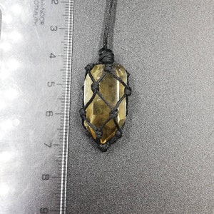 May include: A clear, yellow crystal pendant in a black macrame knot. The crystal is suspended from a black cord.