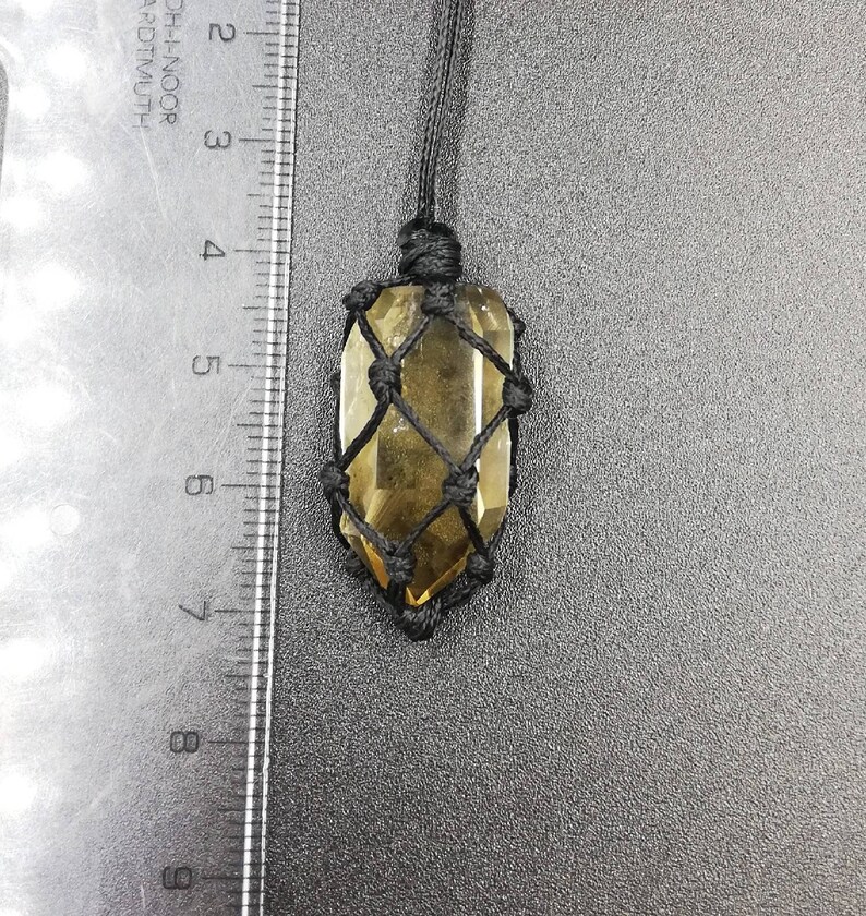 May include: A clear, yellow crystal pendant in a black macrame knot. The crystal is suspended from a black cord.